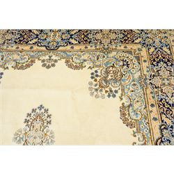 South East Persian Kirman hand-knotted carpet, ivory field with central floral medallion in tones of cobalt and pale blue, issuing scrolling vinery and palmettes, conforming spandrels, main border with scrolling foliage and stylized palmettes, framed by multiple guard borders, with cotton fringe ends 