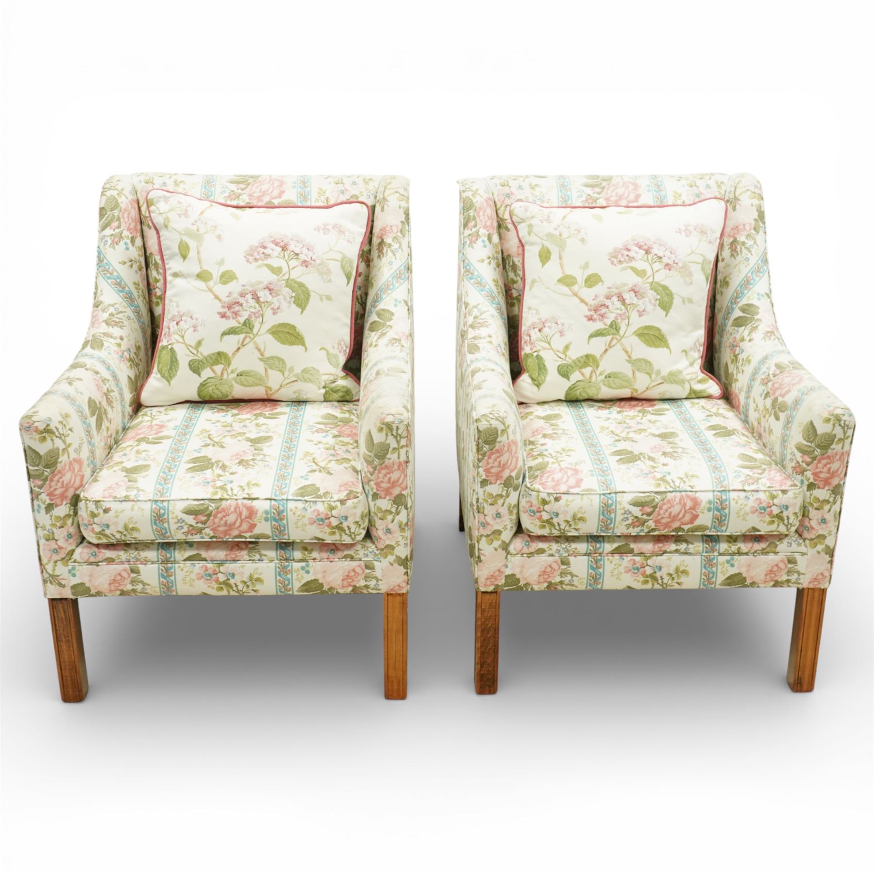 Pair of Edwardian upholstered armchairs, each with shaped padded back flanked by scroll arms, loose seat cushions, upholstered throughout in rose patterned fabric with vertical floral bands, raised on square tapering wooden legs