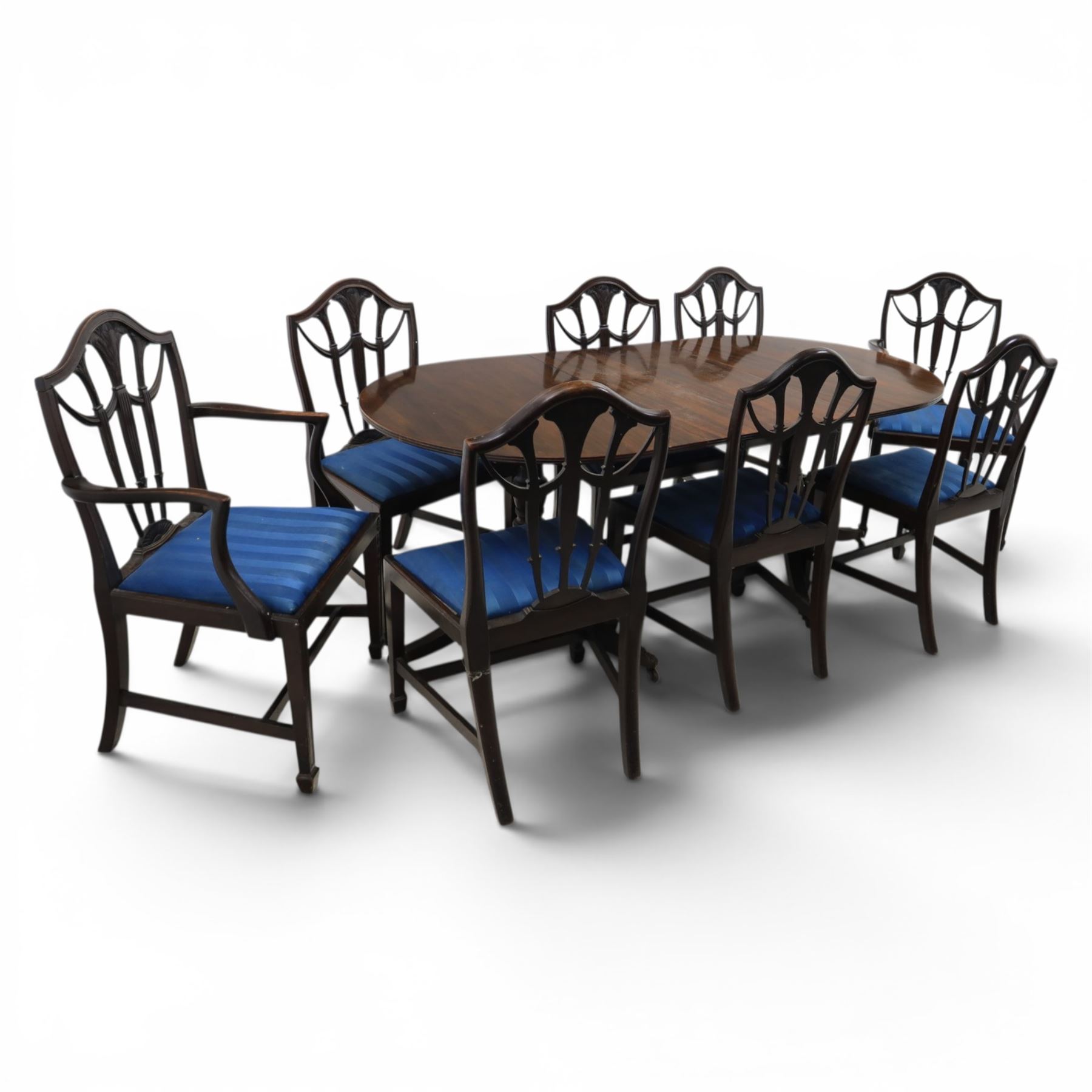 Set of eight George III style mahogany dining chairs, comprising two carvers and six singles, each with shaped top rail above pierced splay carved with feathers, with drop in stuffover seats upholstered in blue striped fabric, raised upon square tapering legs joined by stretchers, together with a mahogany twin pedestal dining table, the oval top with central leaf raised upon turned columns and splayed reeded legs terminating in lion paw feet and brass castors, 