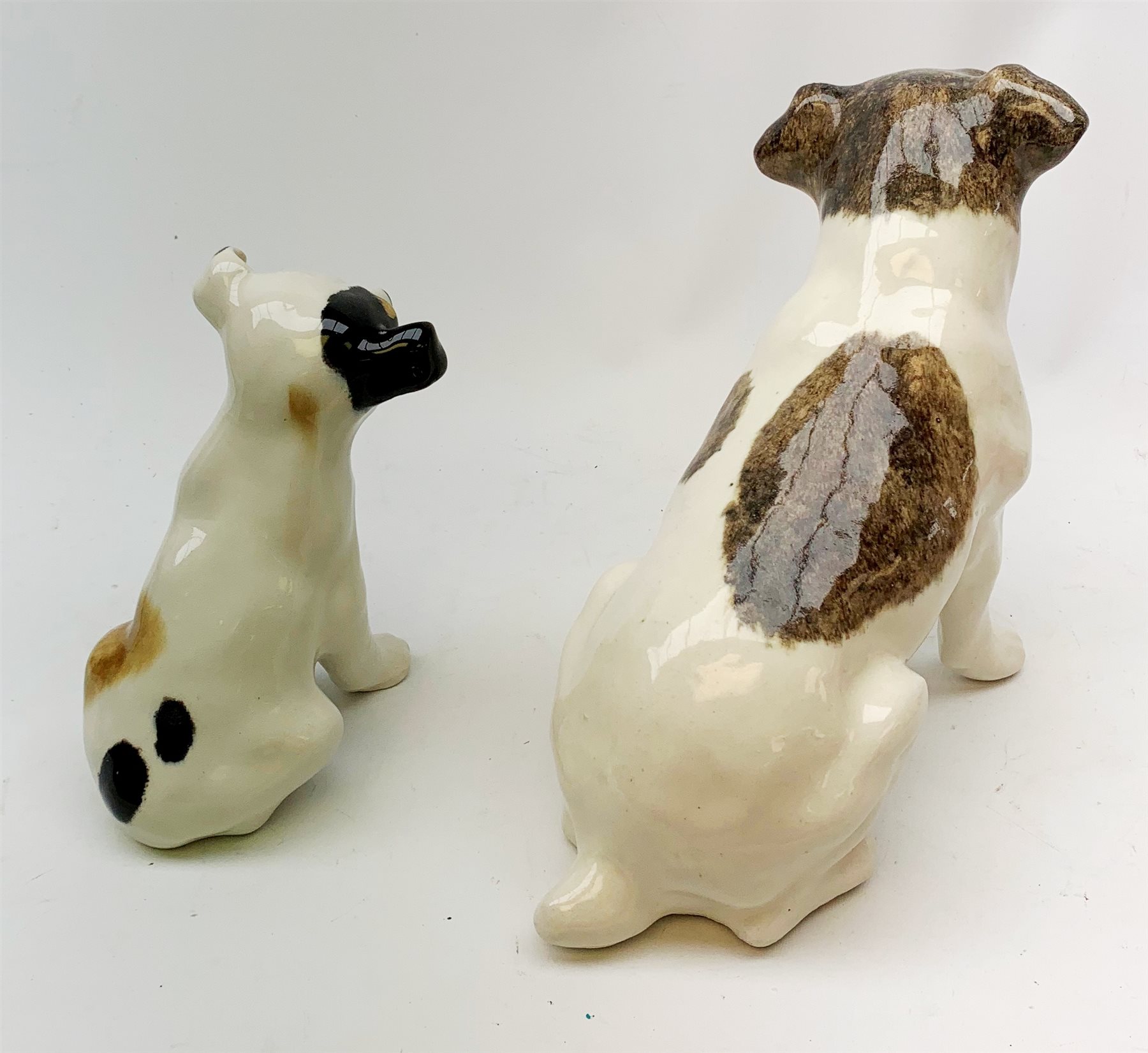 A Winstanley pottery figure modelled as a terrier dog, with inset glass eyes, marked beneath, H28cm, together with another similar smaller example, unmarked, H22cm.