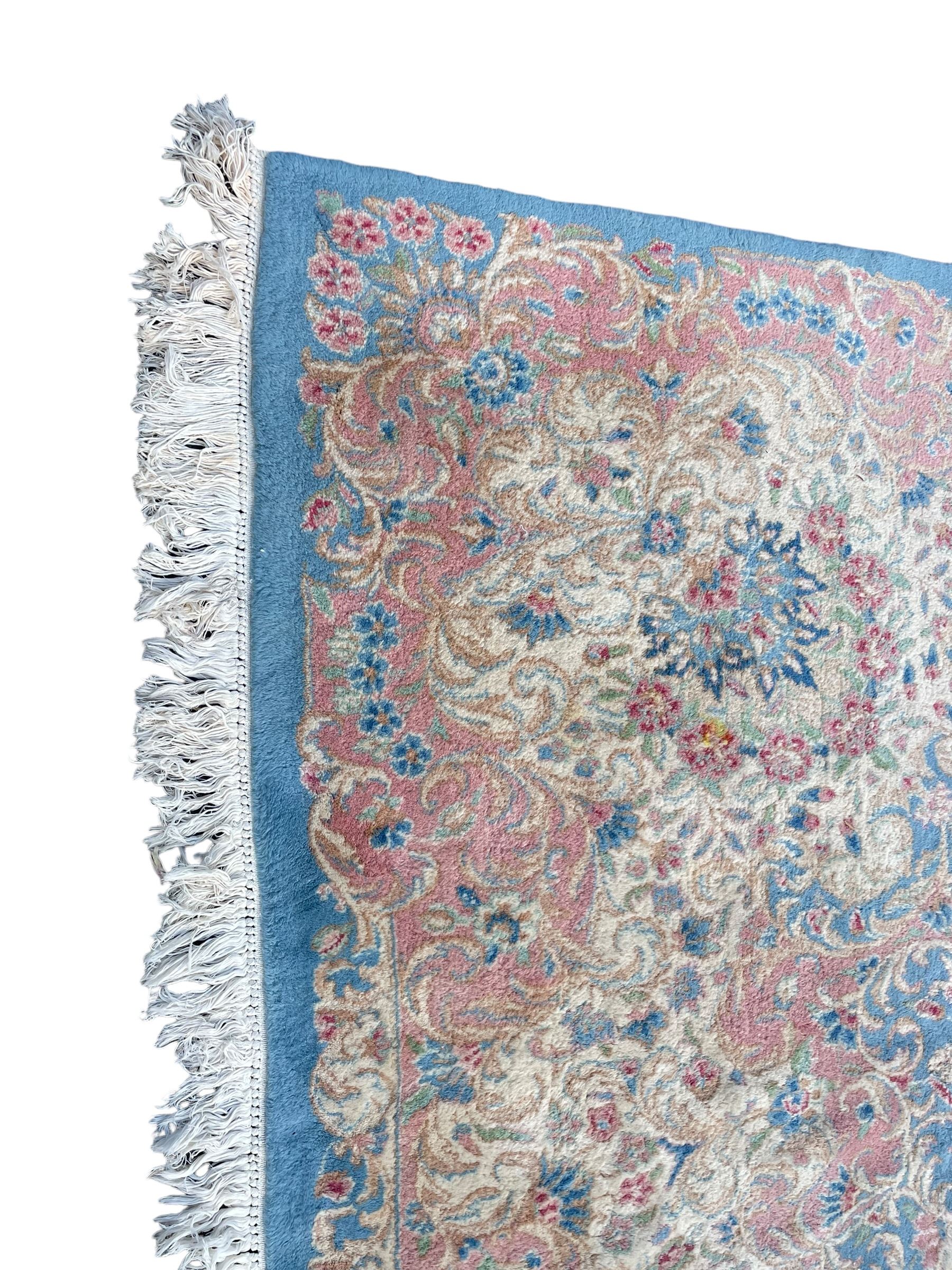 Large Persian design carpet, plain light blue field with floral design central medallion, scrolling foliate spandrels and borders decorated with flower heads