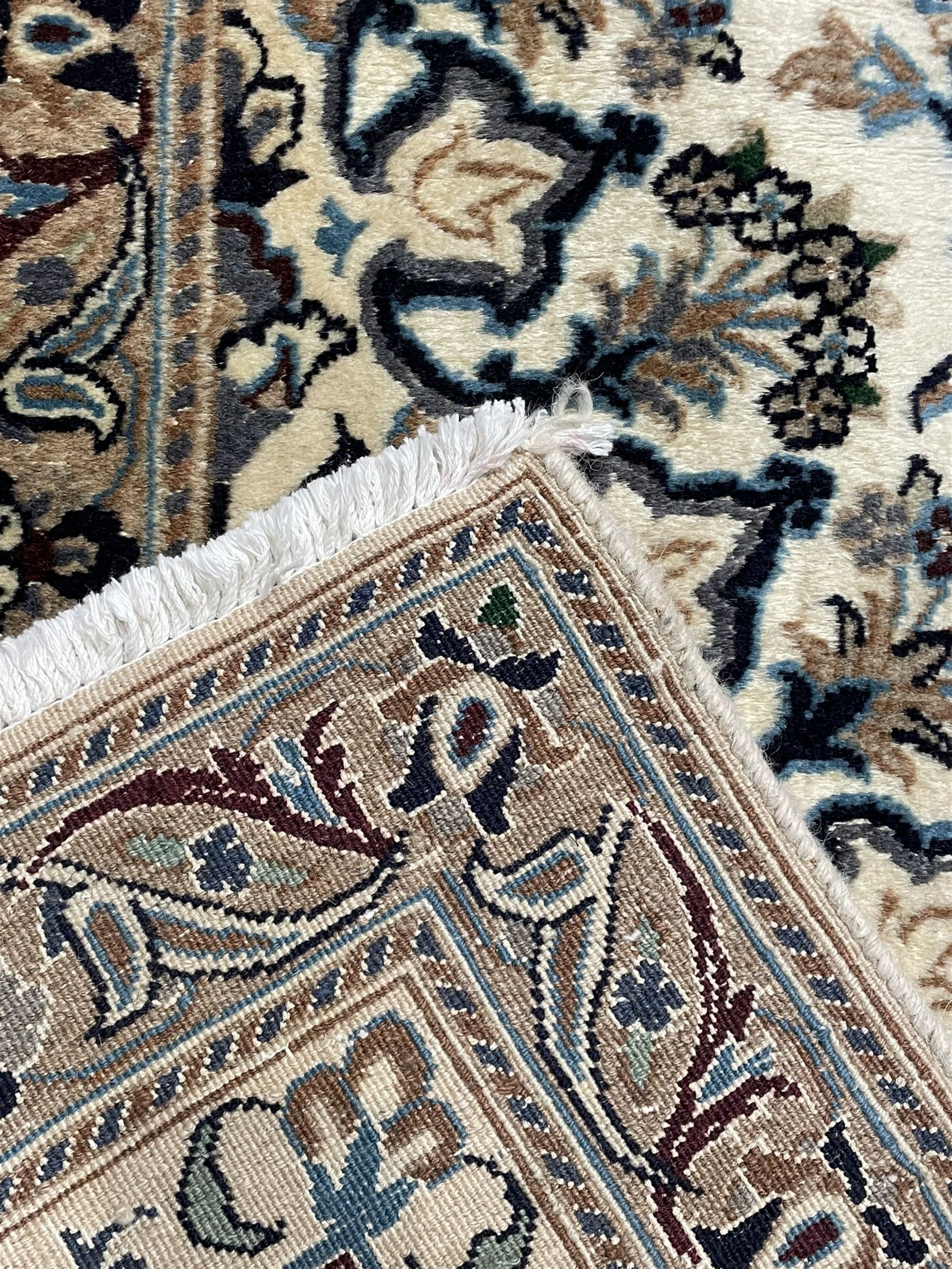 Persian Kashan ivory ground carpet, central rosette medallion surrounded by swirling leafy branches and floral sprays, the main border with scrolling pattern interspersed with floral motifs, within guard stripes 