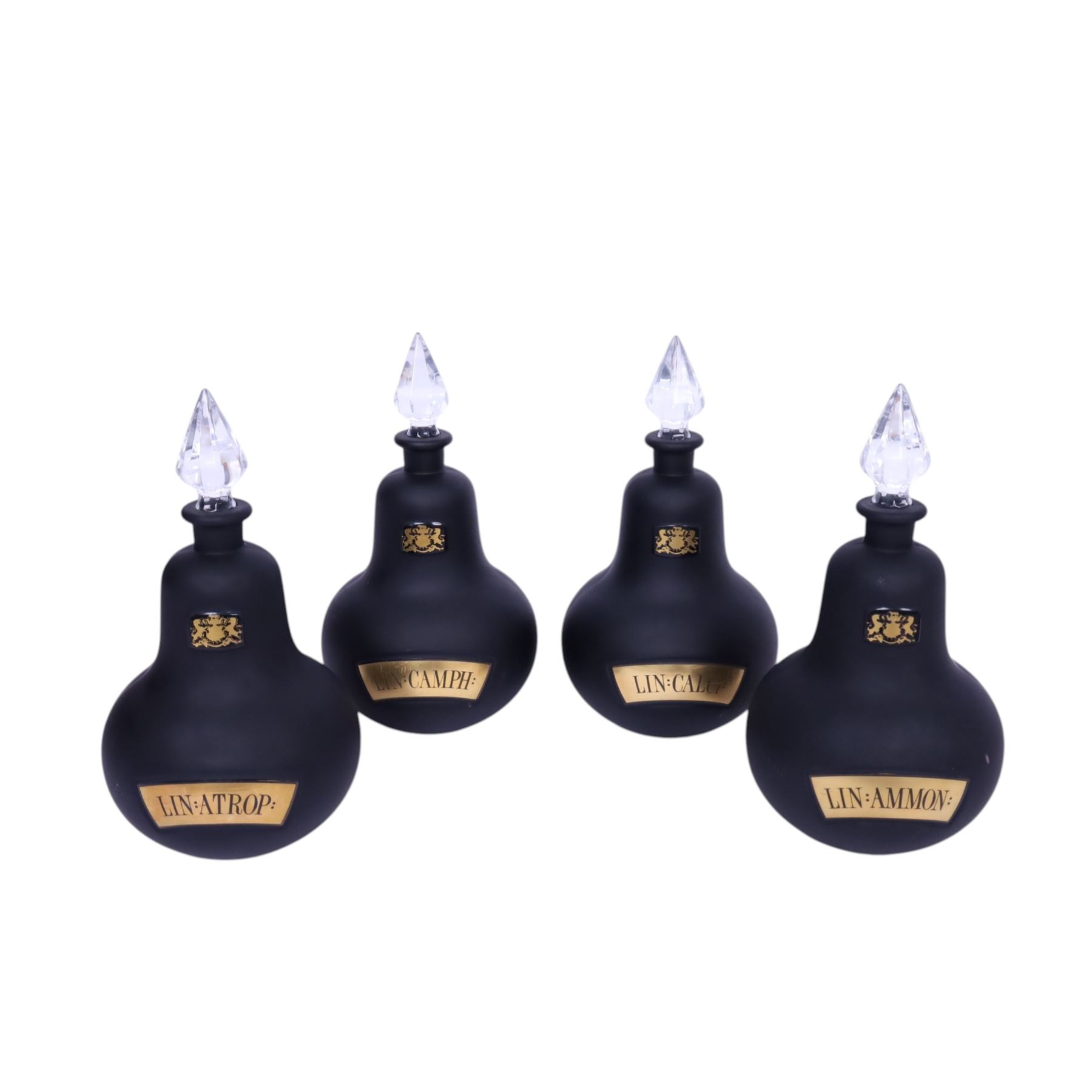 Set of four 20th century Royal Pharmaceutical Society black frosted glass bottles, of bellied form with clear cut glass spire stopper, each body bearing gilt label in Latin: LIN:AMMON:, LIN:ATROP:, LIN:CAMPH:, and LIN:CALCi:, and gilt Royal Pharmaceutical Society crest to neck, H25cm

Provenance: From the collection of the family of Peter Green, a practising pharmacist whose career spanned the mid to late 20th century. During his professional life he managed pharmacies in Yeovil, Somerset, and later Selles Chemist in Filey, North Yorkshire, before purchasing and running his own business, Peter Green Pharmacy, located in the Market Place, Malton. The bottles were displayed as part of the traditional shop fittings in both the Filey and Malton pharmacies and were retained as part of his collection.
