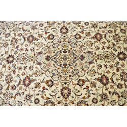 Central Persian Kashan hand-knotted carpet, ivory field with central lobed medallion issuing an all-over design of scrolling vines, palmettes, and floral sprays, within conforming spandrels, enclosed by a foliate border, framed by multiped guard stripes, with cotton fringe ends 