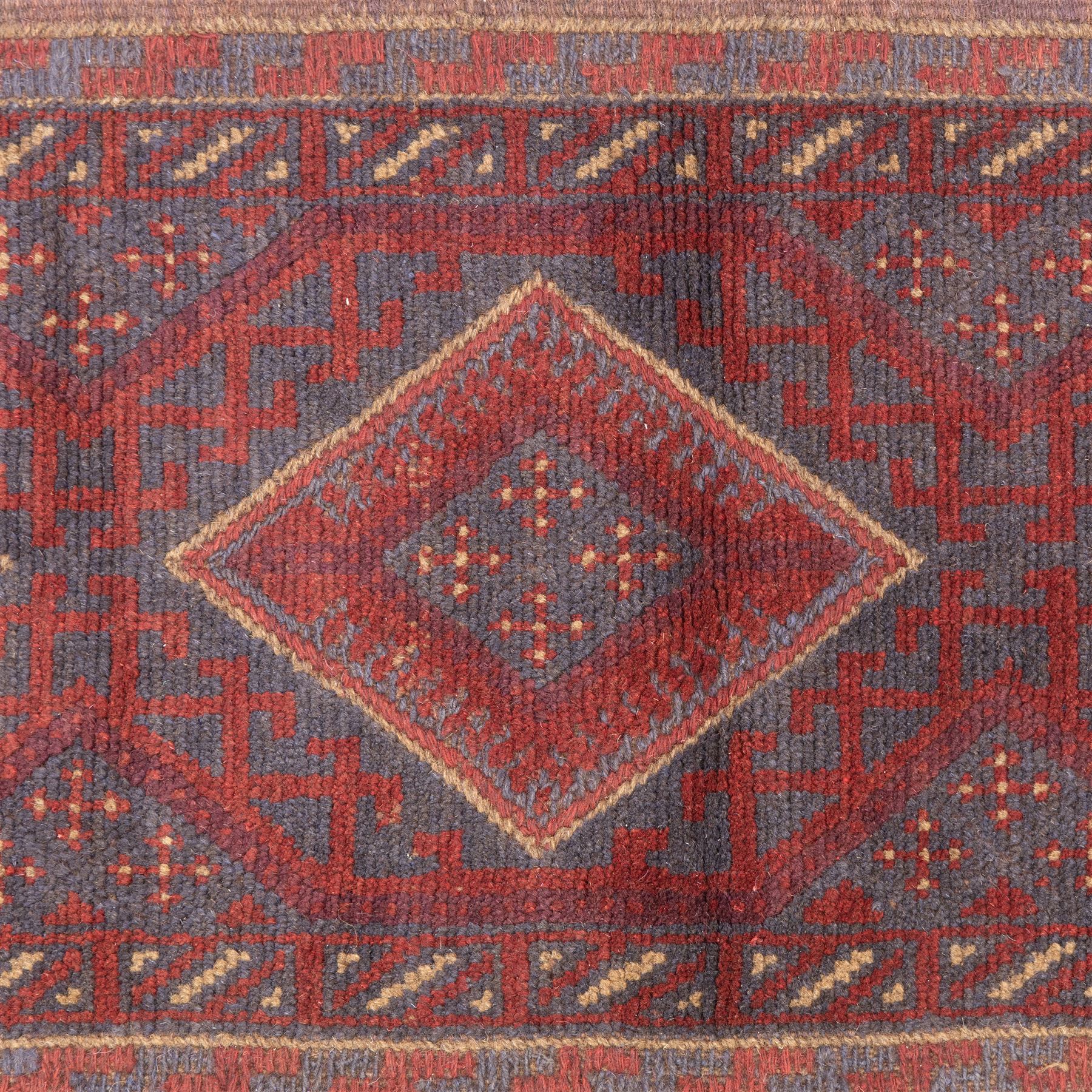Afghan hand-knotted wool runner, dark red and indigo blue madder, with a repeating central diamond medallion design within multiple geometric borders, with flatweave ends 