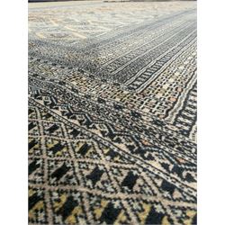 Large Persian Bokhara wool rug, the field decorated with repeating gul motifs in lozenge medallions across a dark ground, enclosed by multiple geometric borders in indigo, ivory and terracotta, from the region of Baluchistan