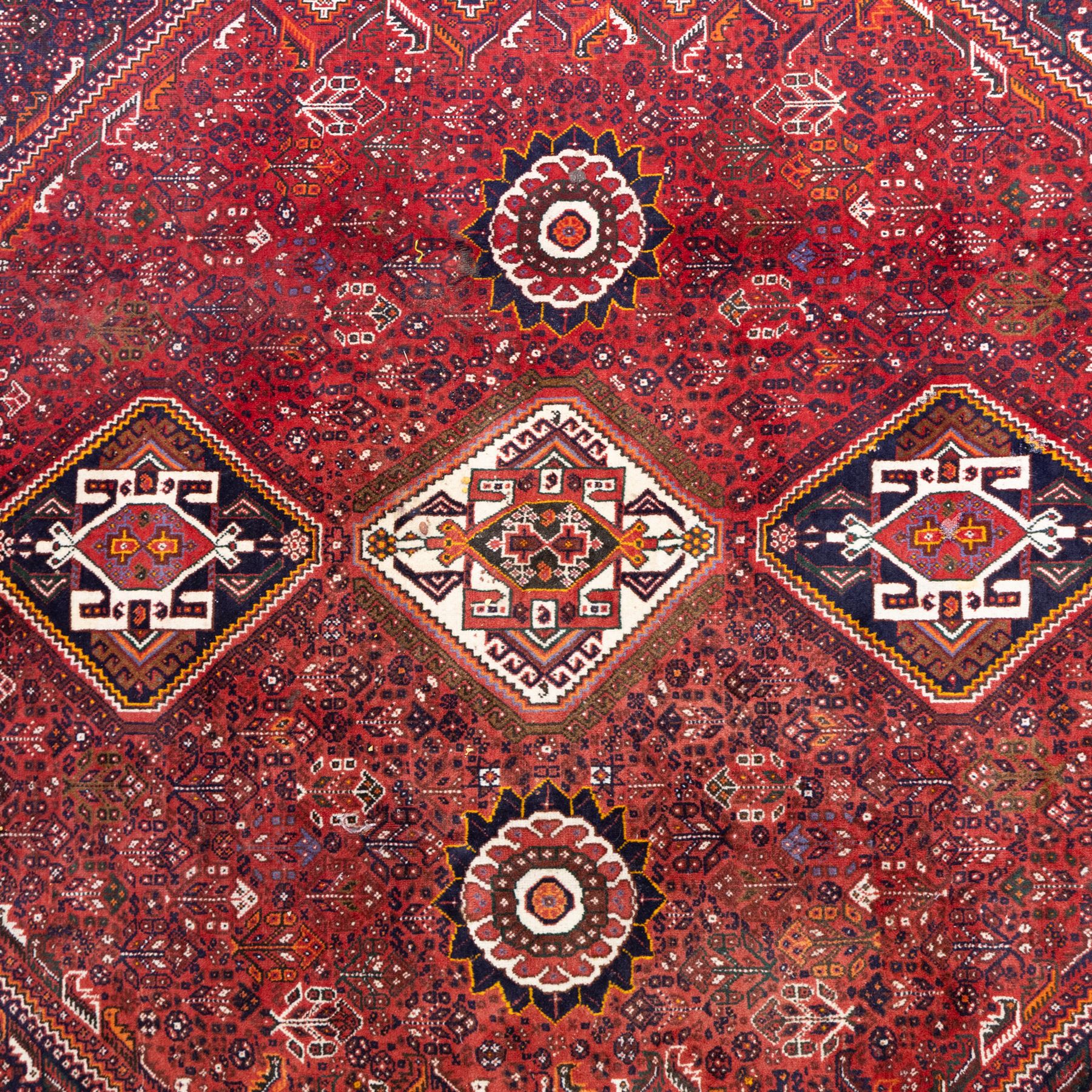 Qashqai wool carpet, red diamond-shaped field decorated with three stepped pole medallions, floral rosettes and scattered stylised motifs, within dark blue spandrels and multiple geometric guard borders