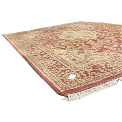 Persian design beige and crimson ground rug, the field decorated with interlacing scrolled foliage, repeating border within guard stripes 