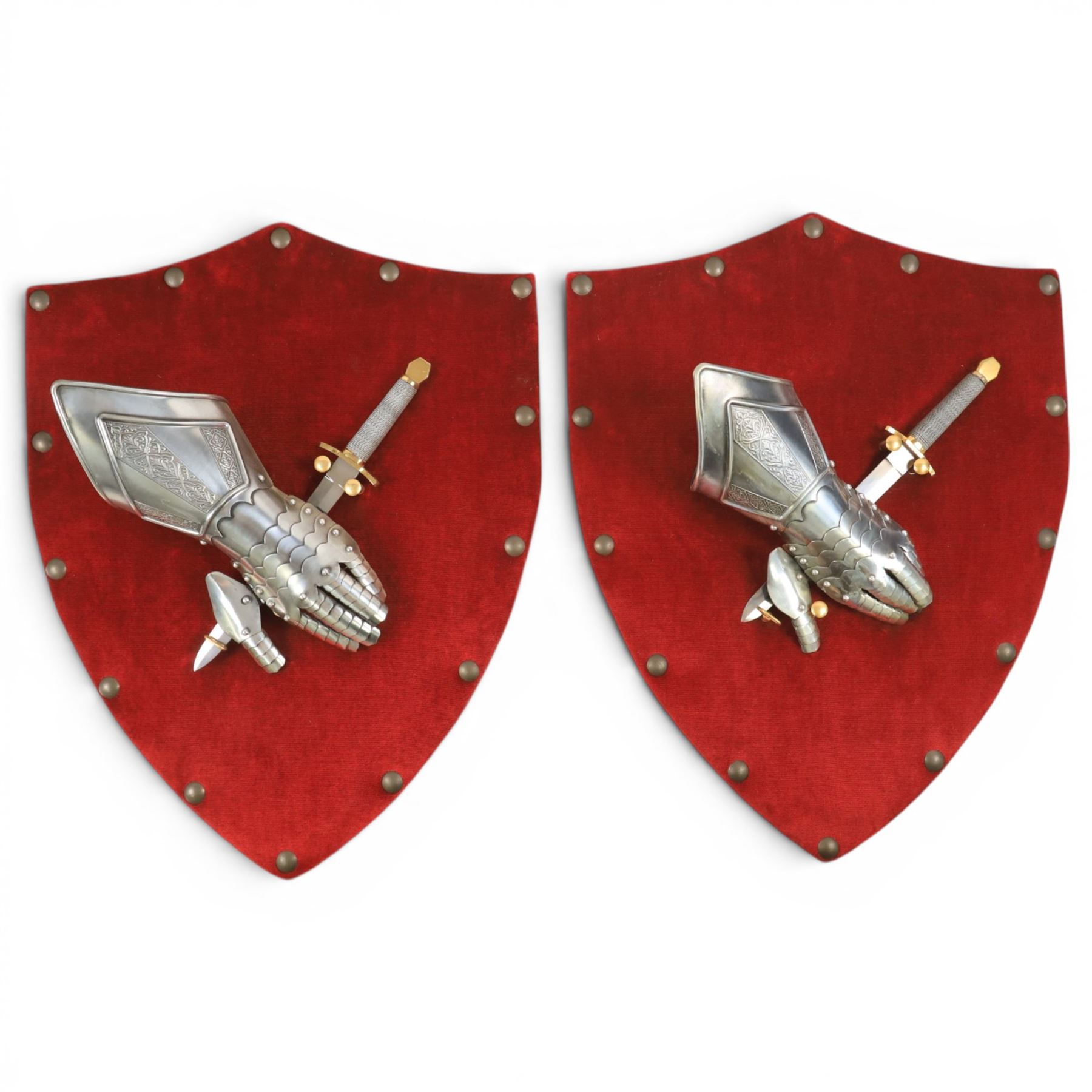 Three replica gauntlets, each housed upon a red wall shield, two with daggers, the third with a sword, largest H102cm