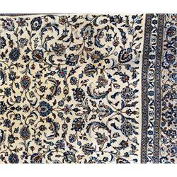 Central Persian Kashan hand-knotted carpet, ivory field with an all-over design of scrolling vines, lotus palmettes, and rosettes in shades of blue and brown within a blue ground border of palmettes and arabesques between multiple guard stripes, 
348 cm x 246cm