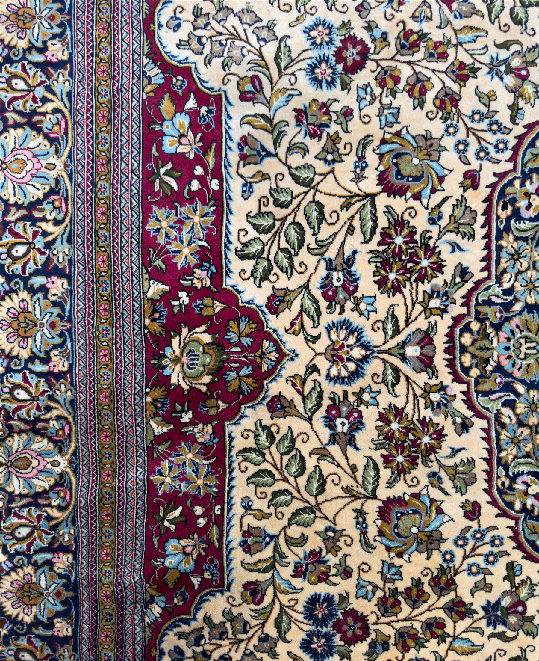 Central Persian Ghom hand-knotted rug, ivory field with scrolling vines, palmettes and flowerheads around a central lobbed medallion with pendants, framed by burgundy spandrels and a navy border of rosettes and arabesques, 289cm x 214cm