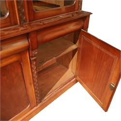 Victorian carved mahogany enclosed bookcase on cupboard, projecting moulded cornice over twin glazed doors enclosing adjustable shelves, flanked by foliate carved uprights, the lower section fitted with two cushion moulded drawers over twin panelled cupboard doors, divided and flanked by conforming carved uprights, on plinth base