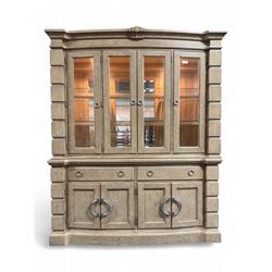 Brunswick - washed oak finish illuminated display cabinet, upper section with four glass-panelled doors enclosing glass shelving, base fitted with two drawers over four paneled cupboard doors, each fitted with distinctive round metal handles, raised on plinth base