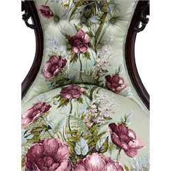 Victorian mahogany framed nursing chair, the waisted back with pierced and scroll carved decoration, upholstered in rose patterned fabric, cabriole supports