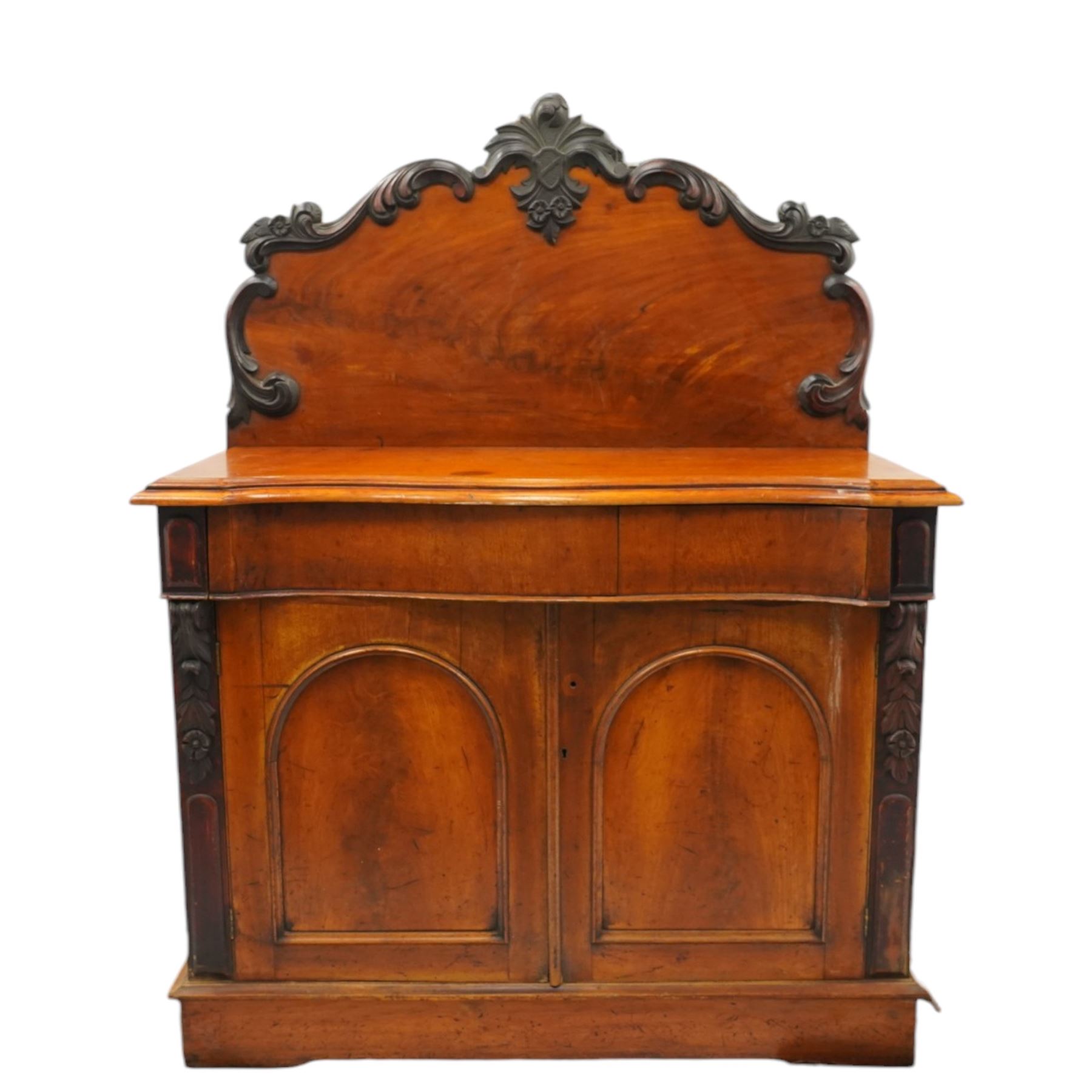 Victorian mahogany chiffonier, raised back with applied carvings, above a serpentine fronted base, a single frieze drawer, above a cupboard with shelf and drawer with campaign handle, raised on a plinth base