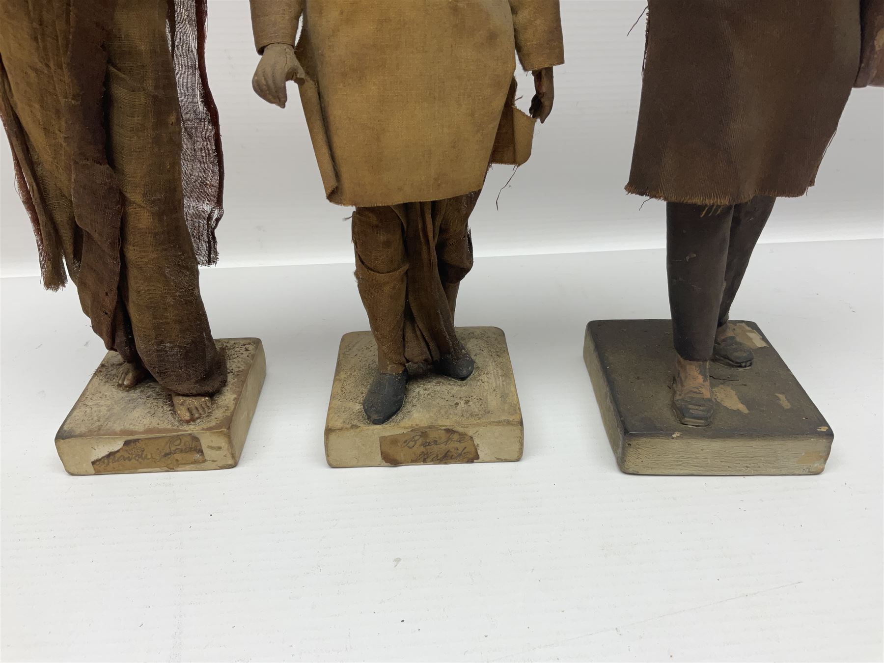 Seven 19th Century Indian clay dolls, possibly Krishnanagar, each figure with painted details, wearing cloth garments, standing on rectangular bases, some with paper label to the base, H25cm