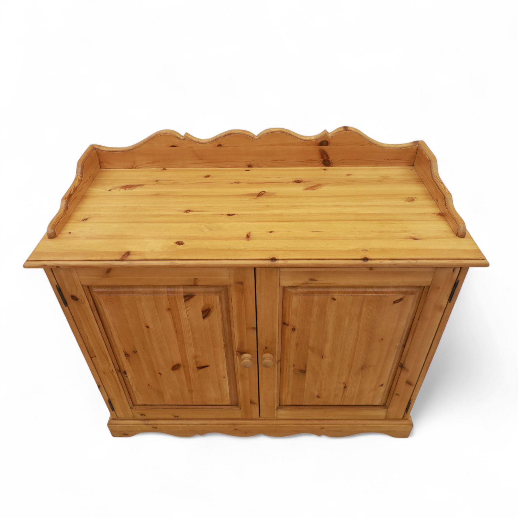 Contemporary pine cupboard, with raised shaped gallery over plain top, panelled double doors below with turned knob handles, shaped apron and plinth base