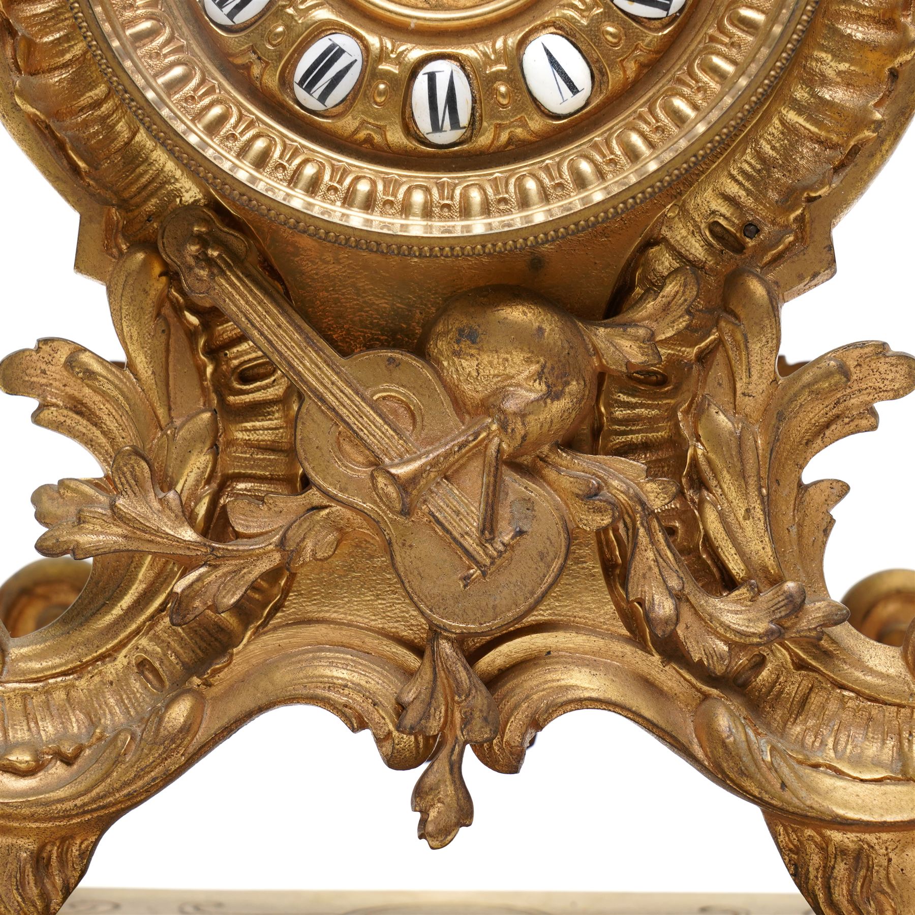 French-Late 19th century 8-day gilt brass rococo style mantel clock, c1890, waisted case  decorated with scroll work, leaves and musical instruments, resting on an attached plinth with splayed feet, dial within a glazed brass bezel with a gilt repoussé centre, porcelain cartouche Roman numerals and steel fleur-di-Lis hands, with a twin train movement, recoil anchor escapement and countwheel strike, sounding the hours and half-hours on a bell. With a matching pair of five-light candelabra. No Pendulum or Key.