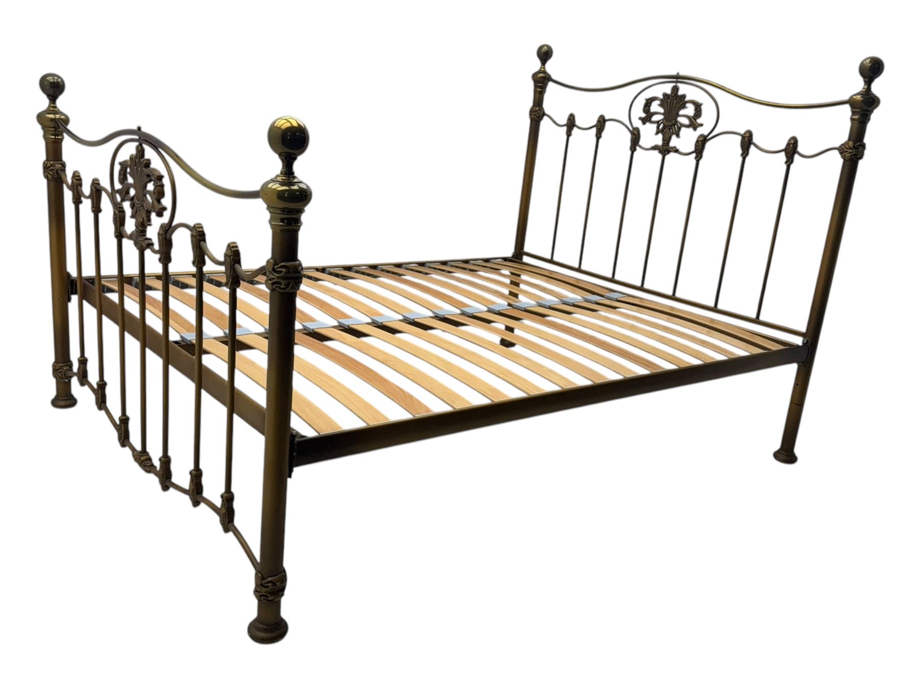 Victorian design king size brass bed frame, featuring an arched headboard and footboard with intricate cast floral and scrollwork centre motifs, flanked by cylindrical supports with ball finials and decorative collars, raised on rounded feet, with a slatted wooden base