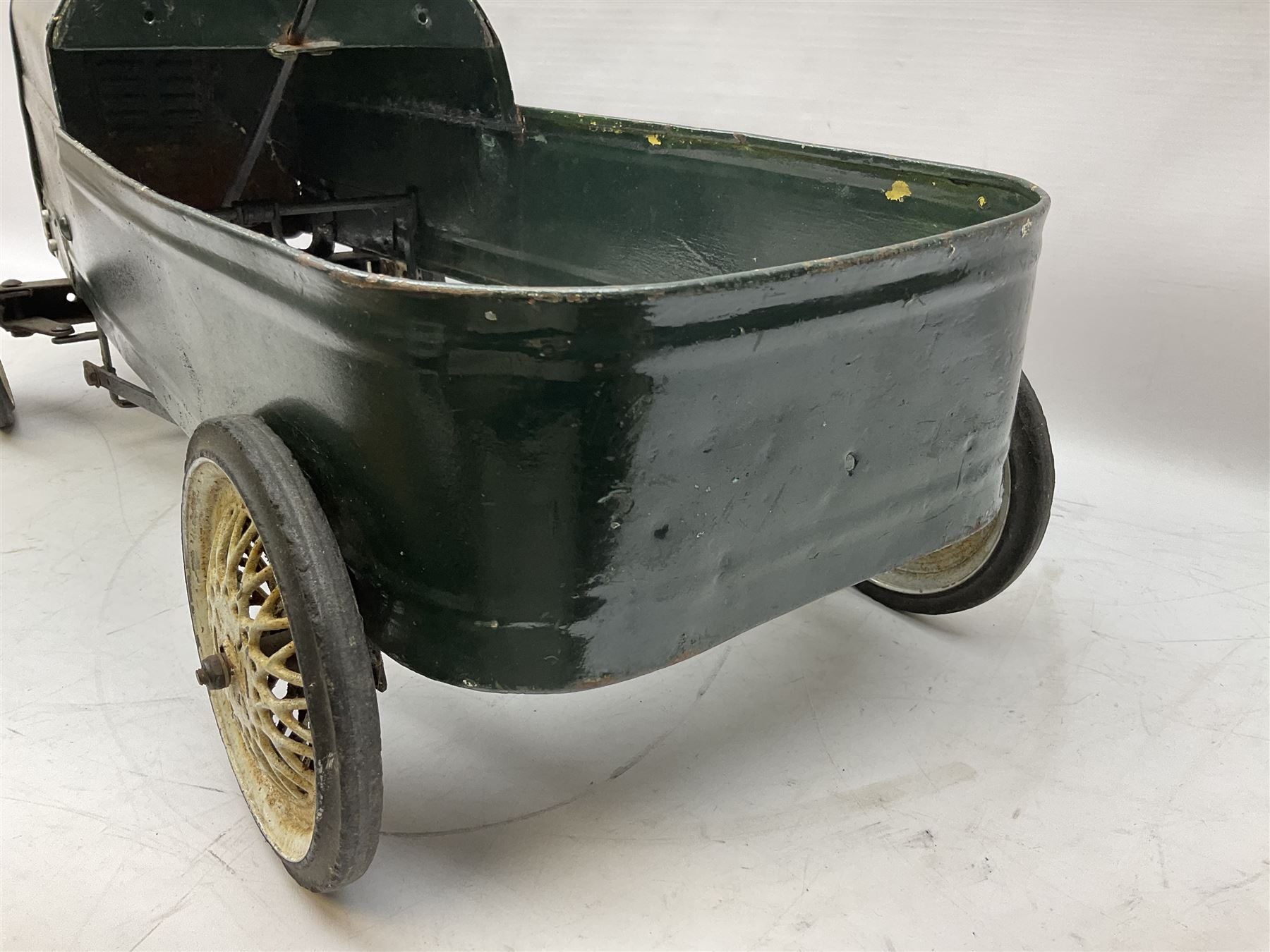 Mid 20th century pressed steel pedal car, the body painted in dark green fitted with pretend radiator to the bonnet, with spoked wheels and rubber tyres, the interior with pedals and steering wheel, L70cm