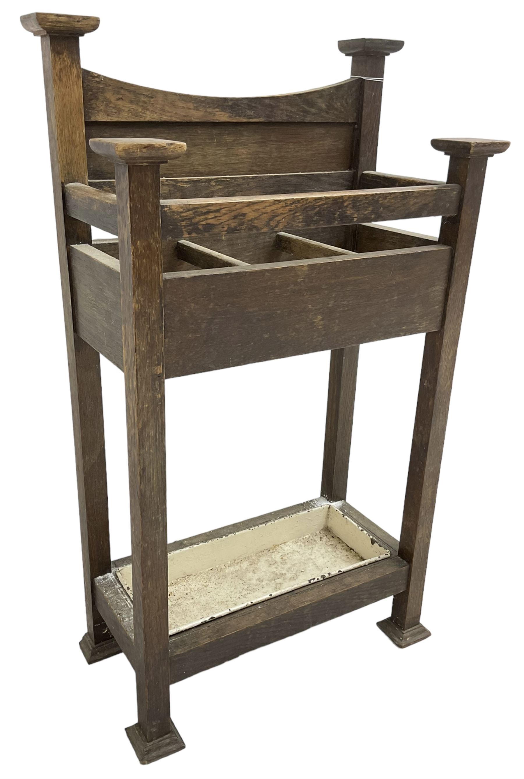 Early 20th century Arts & Crafts oak stick stand, panelled back over three divisions, fitted with metal drip tray, on square supports