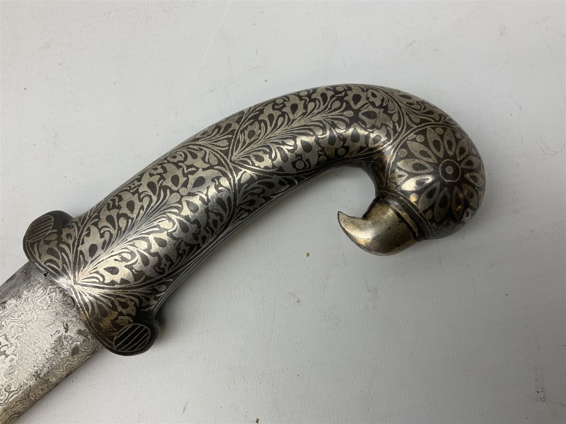 Indian Khanjar dagger with 28cm curving damascus steel blade inlaid with silver floral emblem, white metal and niello style grip in the form of a bird's head with pronounced beak and matching scabbard L44cm overall