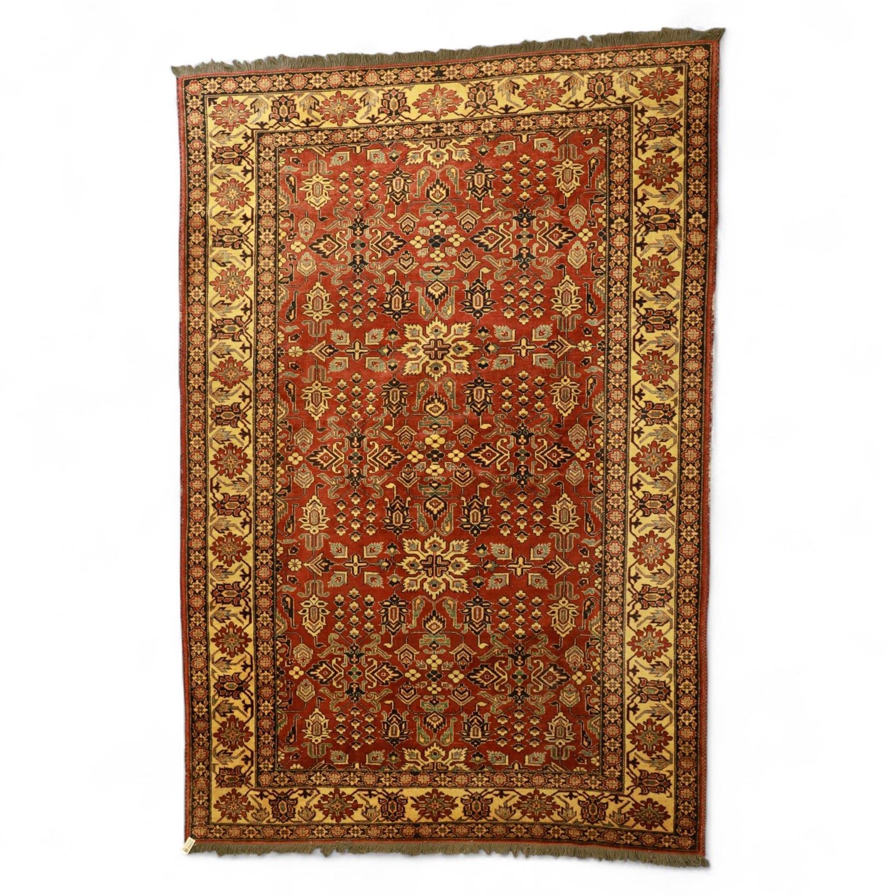 Afghan Gazni Kazak rug, the hand-knotted wool pile featuring a rust red ground with all-over geometric floral motifs in ivory and dark green, enclosed by a wide ivory border with stylised rosettes and angular vine decoration, fringed ends, from the region of Ghazni, Afghanistan