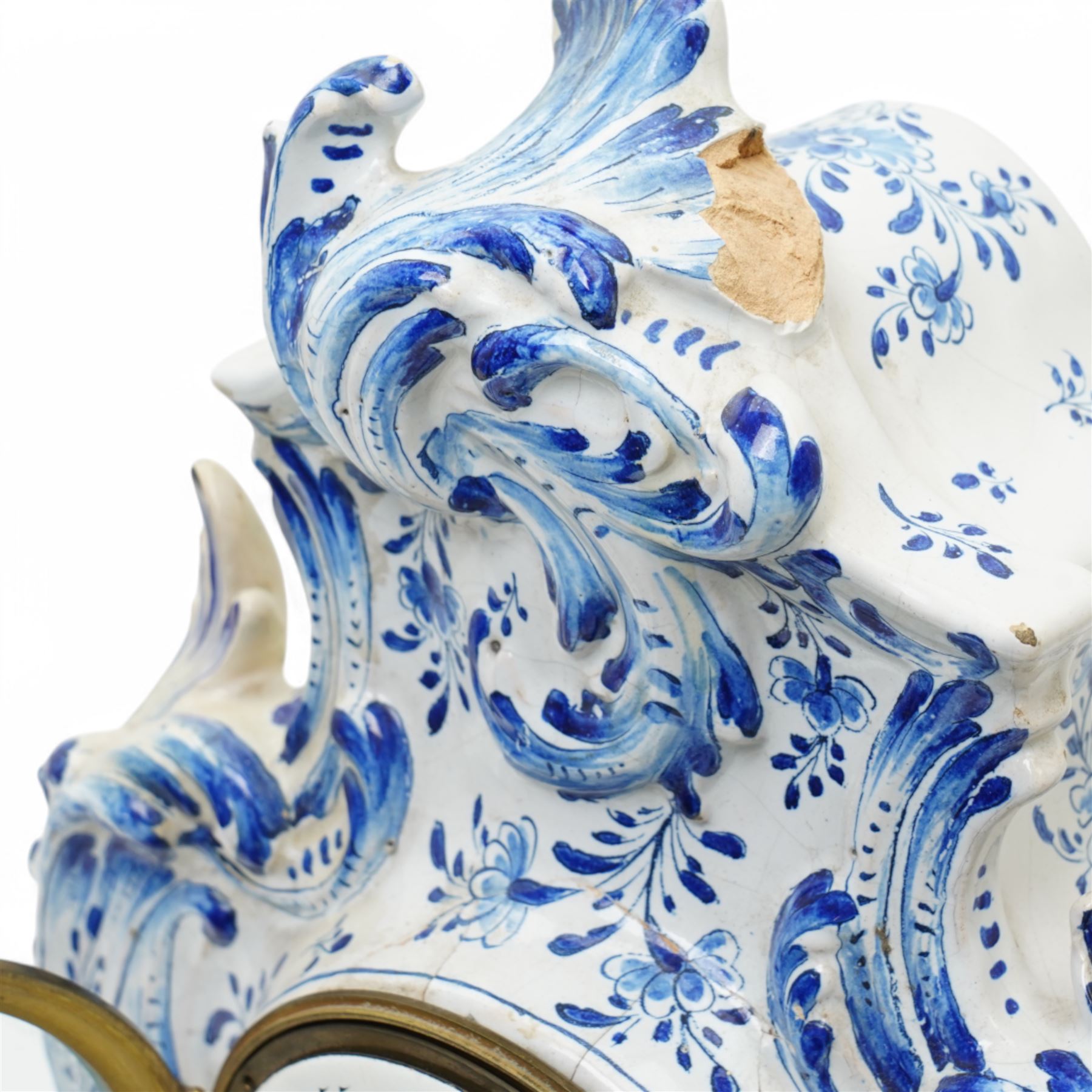 19th century delft blue and white Rococo style 8-day mantle clock, with a scrolling case and floral decoration, depiction of a courting couple in 18th century dress to the front and a contrasting scene of sailing ships on a lake to the rear, with a late 19th-century French twin train movement, enamel dial with Roman numerals, five minute Arabic's and gilt Louis XVI hands within a glazed cast bezel, with a rack striking movement sounding the hours and half-hours on a bell. No pendulum or key.  