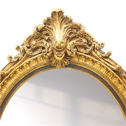 Pair of Rococo Revival gilt framed oval wall mirrors, the exuberant pediment formed of scrolling acanthus leaves and rocaille ornament, the oval bevelled plate set within with ebonised slip with outer repeating lappet decoration, over a rocaille cartouche terminal