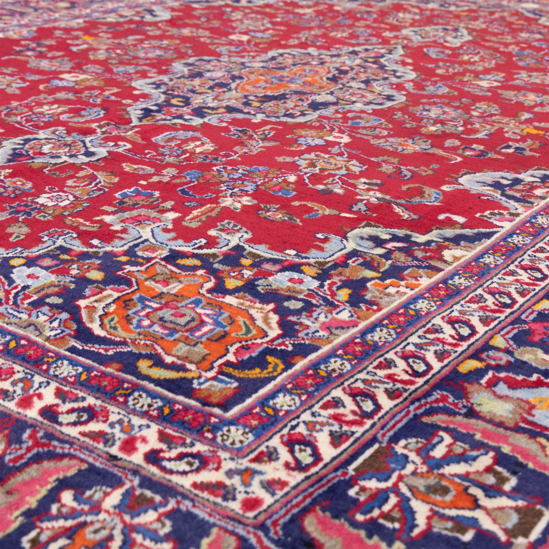 North East Persian Mesued hand-knotted carpet, deep red field with a finely drawn central elongated medallion of navy and ivory, issuing delicate scrolling vines, palmettes and floral sprays in a dense all-over composition, main border on dark ground decorated with a continuous palmette and vine scroll, flanked by multiple narrow guard stripes incorporating rosettes and stylized floral devices, with cotton fringe ends 
