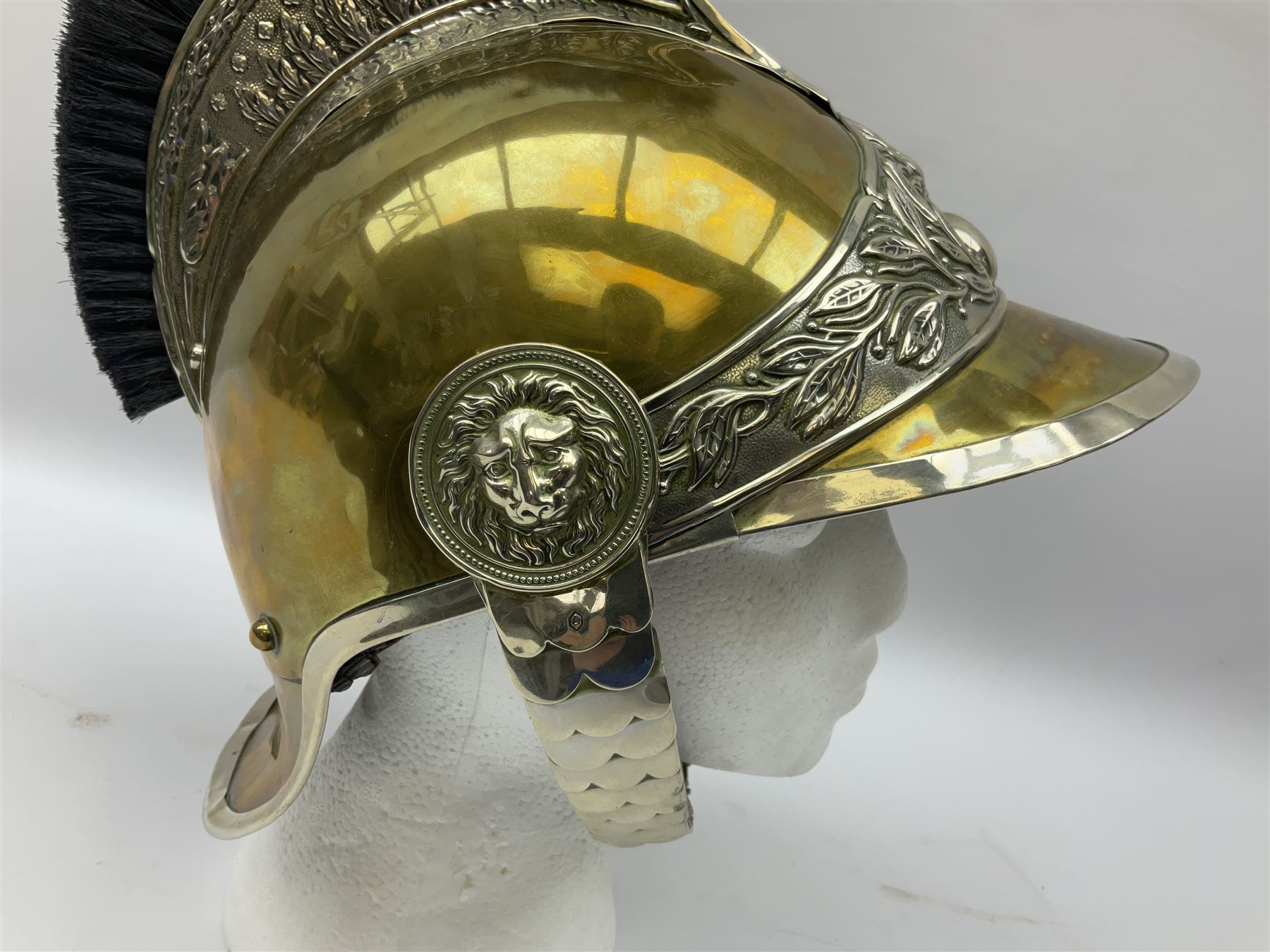 Early 20th century French mounted gendarme's helmet, brass with nickel-silver mountings, broad band embossed with fused grenade, high comb with the face of the gorgon Medusa at the peak and with a black horse hair crest, plume socket at the left, leather-backed nickel-silver chin scales with lion mask mounts.