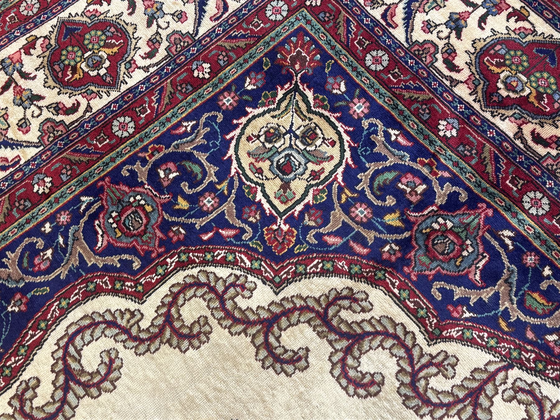 Northwest Persian signed Tabriz ivory ground carpet, central medallion with intricate floral motifs, the field and spandrels decorated with scrolling tendrils and palmettes, ivory main border with crimson and indigo floral decorations, surrounded by crimson guard bands