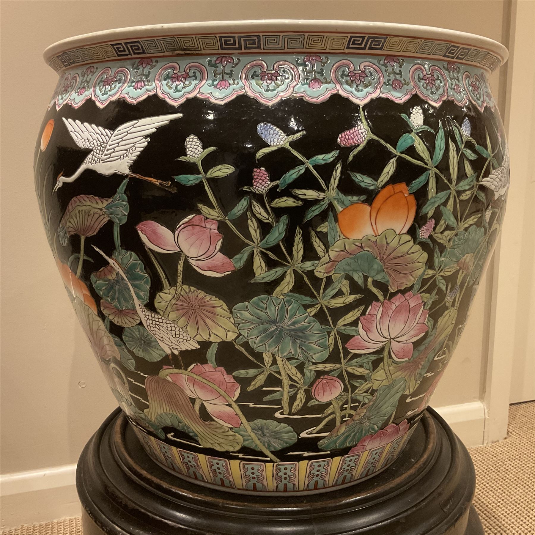 Large 20th century Chinese famille noir glazed porcelain jardinière, of ovoid form, the exterior enamelled with butterflies and white cranes amidst blossoming water lilies and pads against a black ground, between two stylised polychrome borders and beneath a key border to rim, the interior enamelled with red koi fish swimming amongst water fronds and weeds, with printed red character mark beneath, the whole upon an ebonised hardwood stand with three cabriole legs, jardinière H42cm D47cm, including stand overall H69.5cm