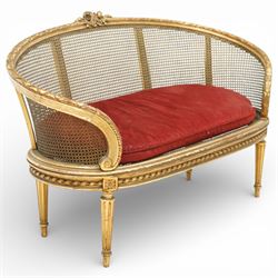 19th century giltwood and gesso settee, with shaped crest rail centred by carved floral detail, the cane back with vertical divisions, upholstered seat with loose cushion, raised on fluted tapering legs