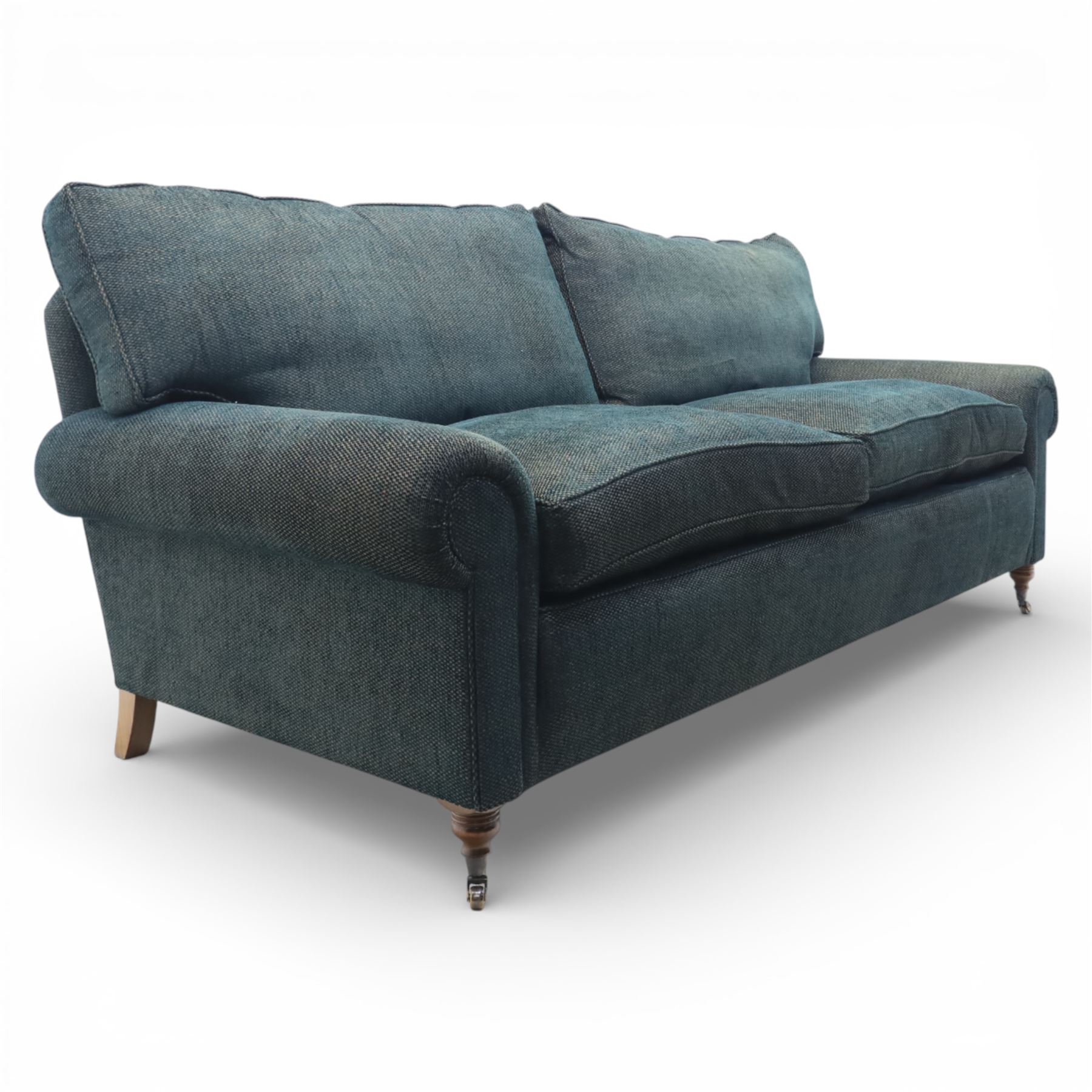 Late 20th century three seat sofa upholstered in green fabric, with gently rounded scroll arms, loose seat and back cushions, raised on turned wooden legs with castors, rear splayed legs