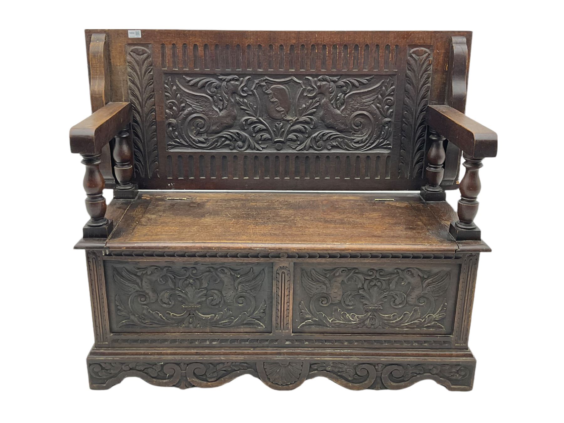 Late 19th century oak monk's bench, the hinged back or top carved with mythical winged dragons, central cartouche and scrolling acanthus leaves, on turned supports, hinged box seat revealing storage, the panelled front matching the back, shaped bracketed skirt carved with shell and scrolled leafage