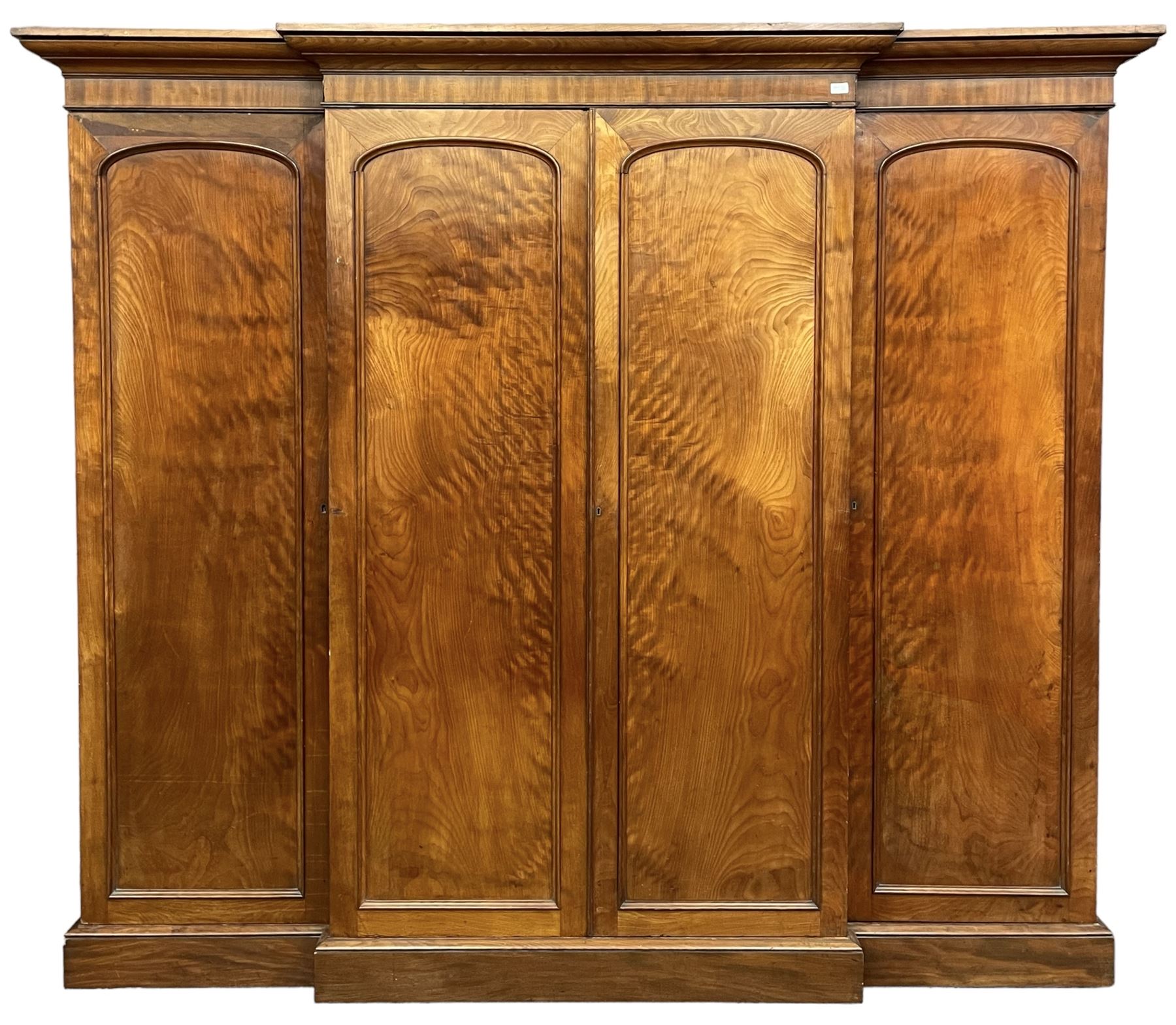 19th century figured mahogany quadruple breakfront press wardrobe, projecting cornice with banded frieze over arch panelled doors, the interior fitted with three sliding trays over two short and three long graduating drawers with recessed brass handles, flanked by two hanging cupboards with hooks