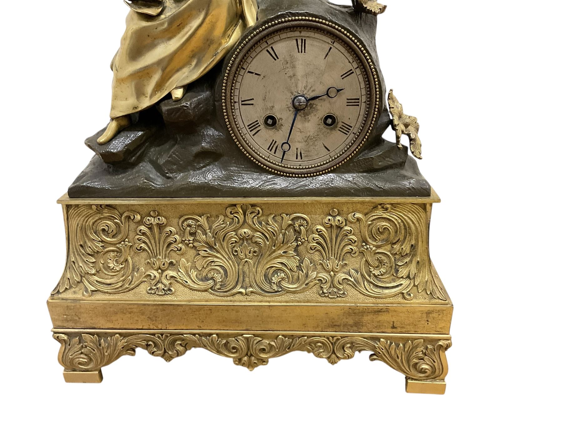 French-Louis XVIII  8-day mantle clock c1820, on a rectangular gilt metal base incorporating repeating cast leaf decoration on a pierced apron and bracket feet, surmounted with a cast brass figure depicting a reclining lady in 18th century dress, Parisian drum movement with a silk suspension and unglazed silvered dial, with Roman numerals and steel moon hands, dial pinned to a countwheel striking movement, sounding the hours and half-hours on a bell. With pendulum and key.
