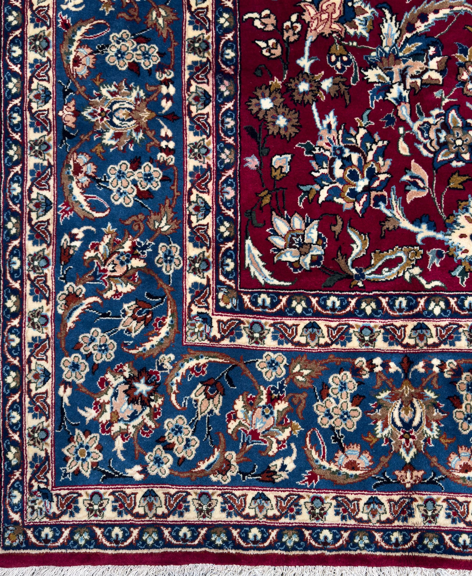 Central Persian Yazd hand-knotted rug, madder red field with scrolling vines, palmettes, and rosettes around a cusped lozenge medallion within a blue ground border of palmettes and flowerheads, 366cm x 250cm