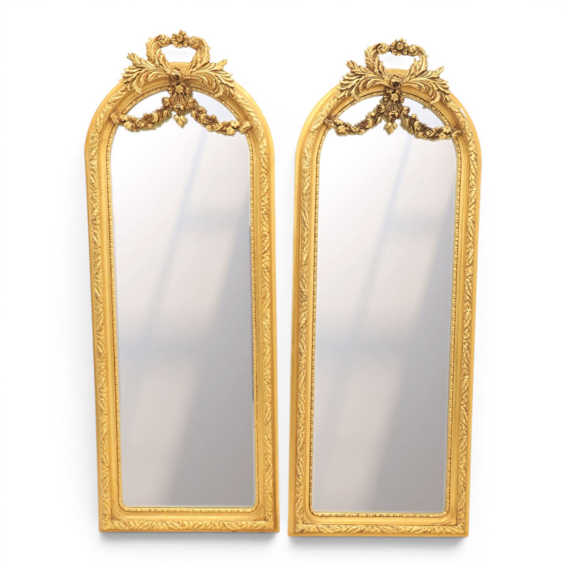 Louis XVI style giltwood pair of wall mirrors, arched frames with moulded borders, surmounted by ribbon tied floral crestings and trailing husk swags, enclosing bevelled mirror plates