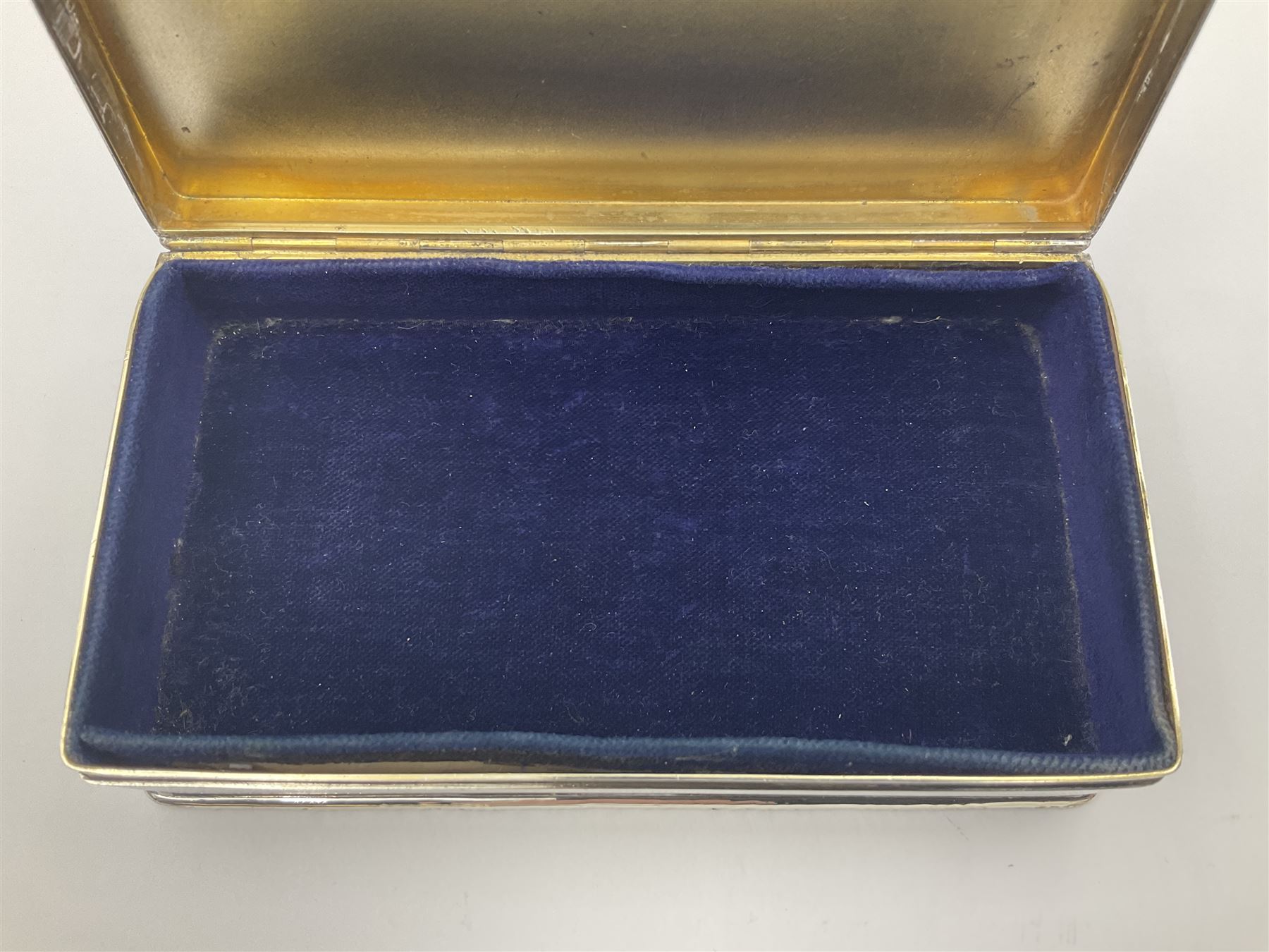 1920's silver table cigarette box, of rectangular form with engine turned decoration to the exterior, the hinged cover with central vacant rectangular panel and raised foliate rim, opening to reveal a gilt interior with later plush lining, hallmarked Charles Henry Dumenil, London 1923, H3.5cm L14.5cm D8.5cm