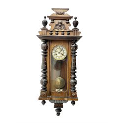 German - late 19th century mahogany and ebonised 8-day wall clock, with a shaped pediment, applied carvings and finials, fully glazed door with visible gridiron pendulum flanked by turned half columns , curved base with finials below, two part enamel dial with Roman numerals and pierced steel hands, count wheel striking movement sounding the hours and half hours on a coiled gong. With key. 