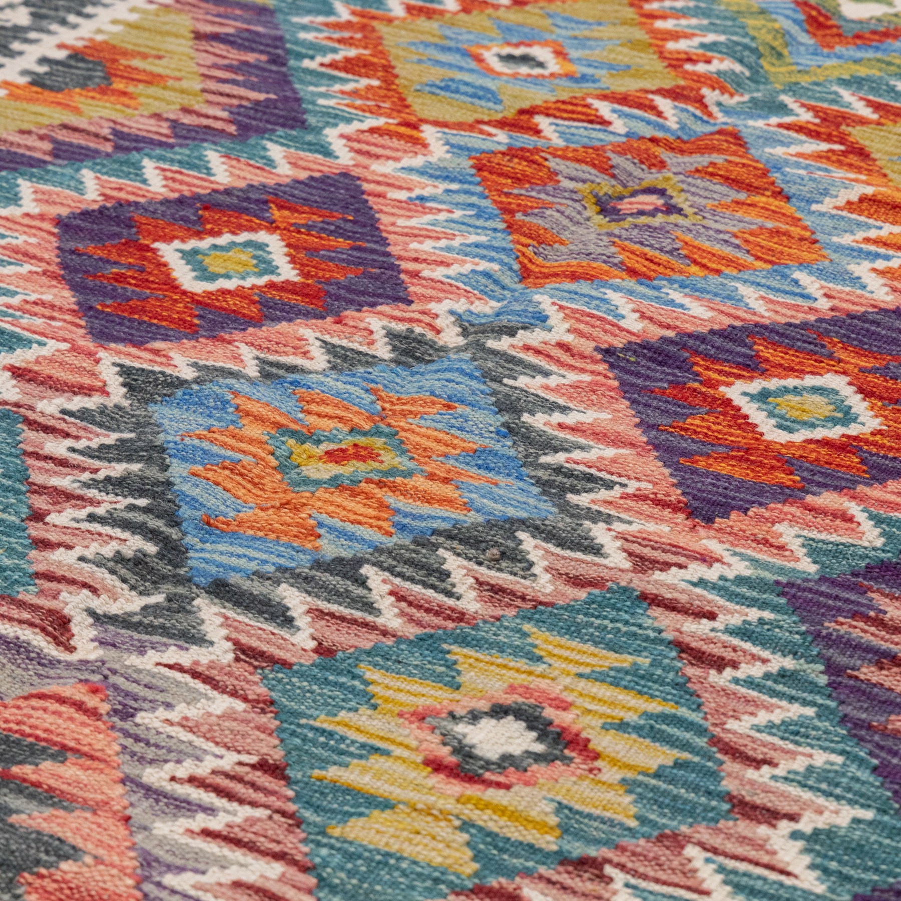 Afghan kilim multicoloured rug, the geometric field decorated with repeating lozenges of contrasting tones heightened with ivory outlines, the outer guard band with repeating hooks and Vitruvian scrolls