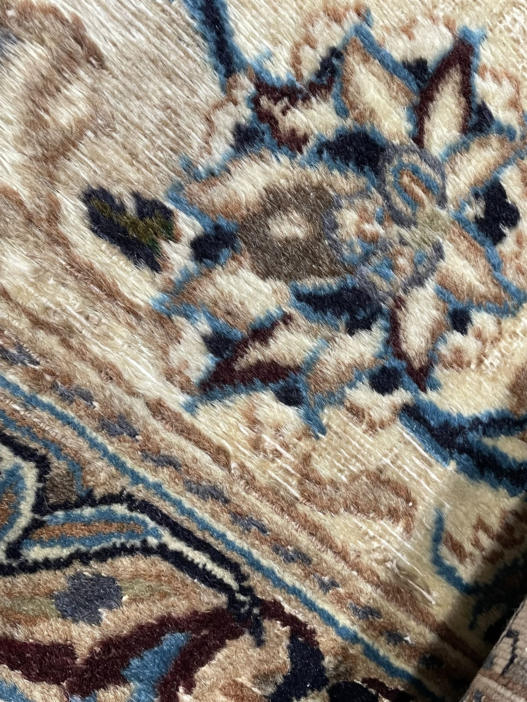 Persian Kashan ivory ground carpet, central rosette medallion surrounded by swirling leafy branches and floral sprays, the main border with scrolling pattern interspersed with floral motifs, within guard stripes 