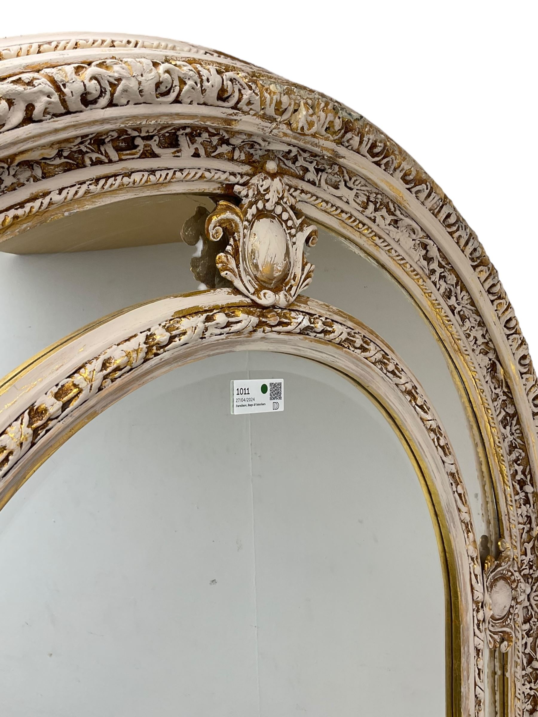 Large painted and gilt arched wall mirror, the frame decorated with scrolling leafy branches, central bevelled mirror mirror surrounded by plain panels, decorated with cartouche mounts 