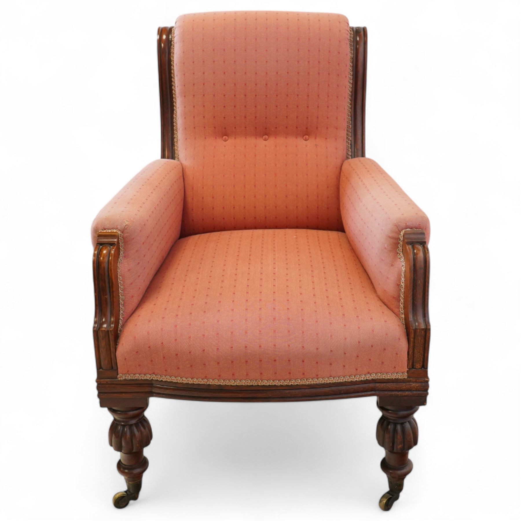 Victorian mahogany framed armchair, upholstered in salmon pink dot patterned fabric, the moulded arms with carved scroll terminals, raised on turned and fluted front legs and swept back legs, all with castors