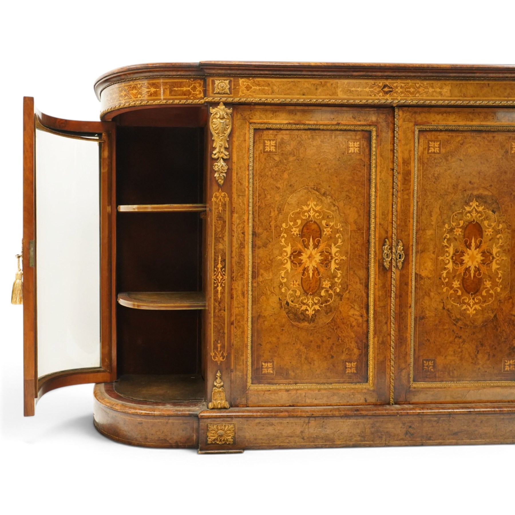 Large fine Victorian figured and burr walnut credenza, the breakfront D-shaped top with moulded edge, over an ornate frieze with inlaid Aesthetic Movement scrolling and geometric ornament, applied with gilt-metal ribbon-twist moulding and mounts, the central panelled doors profusely inlaid with scrolling foliate motifs and stringing, flanked by gilt-metal cartouche and scrolling acanthus corbel mounts, with flanking glazed bow-front side doors, on skirted base with further gilt metal foliate mounts