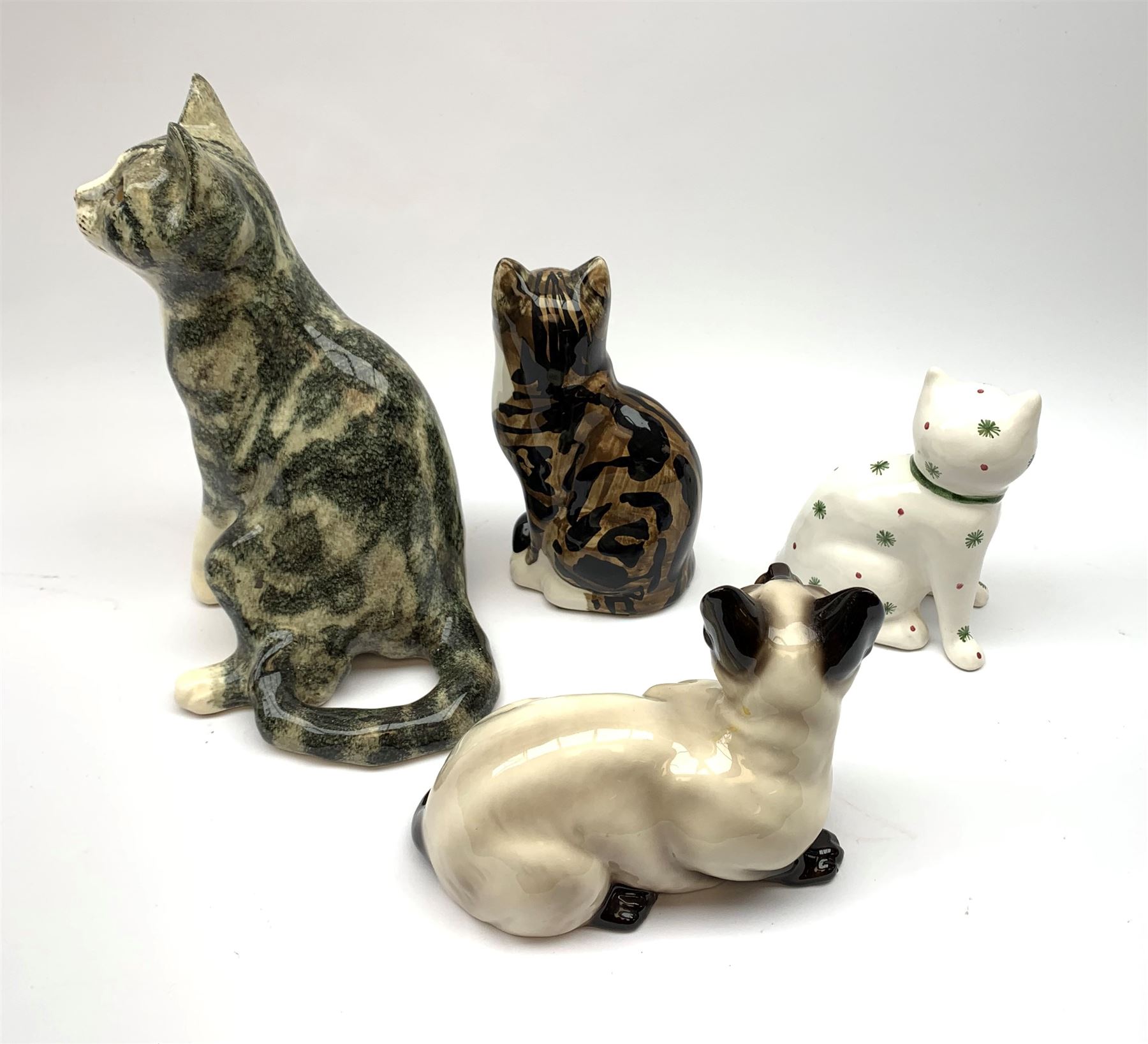 A Winstanley cat, with glass eyes in seated post, signed beneath, H25cm, together with three other figures of cats, including a Rye Pottery example. (4). 