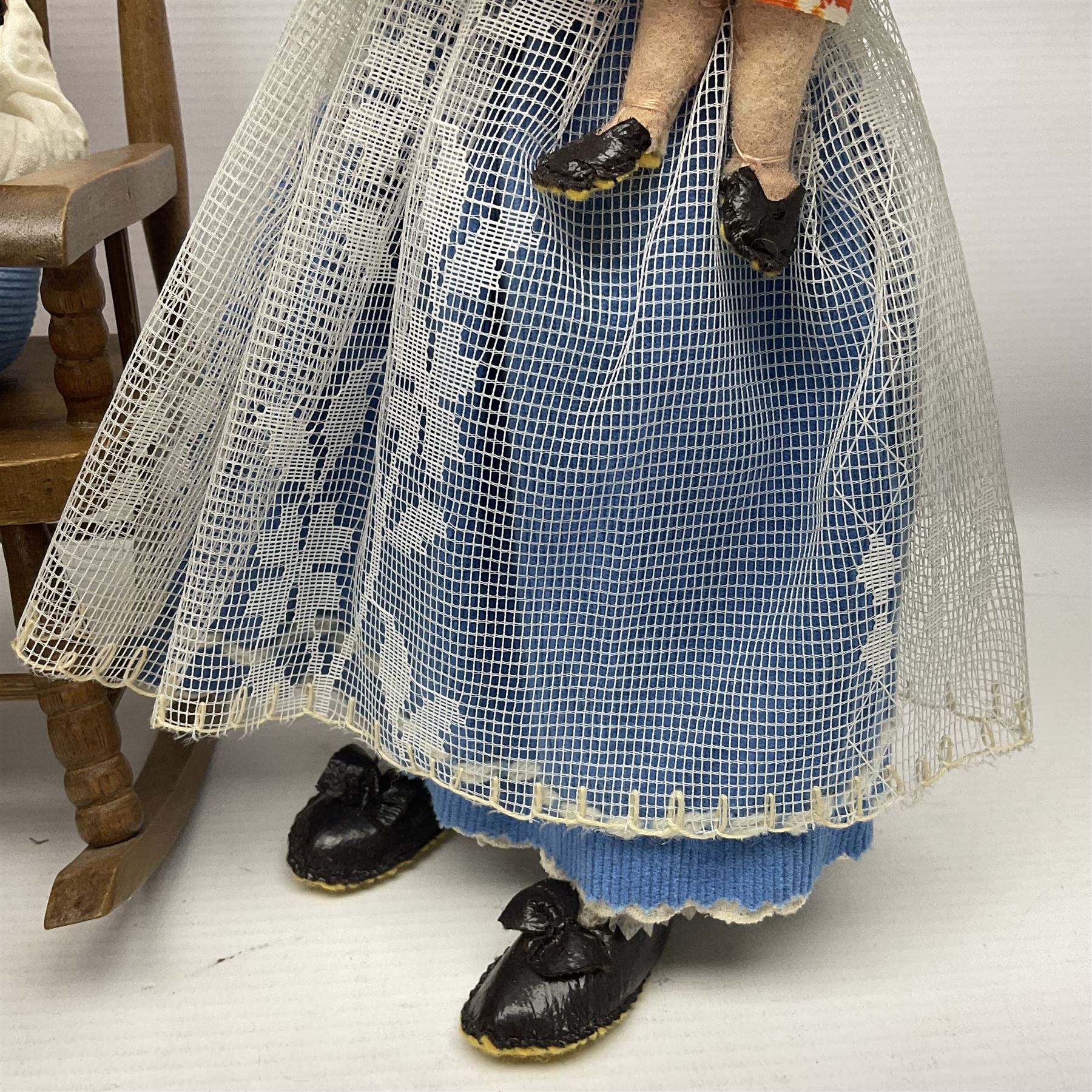 Anna Meszaros Hungary - three hand made needlework figurines - 'The Cobbler' as a child seated in a wooden rocking chair working on a removed boot H24cm; young girl standing crying holding a doll with broken head H32cm; and young girl in long dress and bonnet standing holding a doll H27cm (3)  Auctioneer's Note: Anna Meszaros came to England from her native Hungary in 1959 to marry an English businessman she met while demonstrating her art at the 1958 Brussels Exhibition. Shortly before she left for England she was awarded the title of Folk Artist Master by the Hungarian Government. Anna was a gifted painter of mainly portraits and sculptress before starting to make her figurines which are completely hand made and unique, each with a character and expression of its own. The hands, feet and face are sculptured by layering the material and pulling the features into place with needle and thread. She died in Hull in 1998.