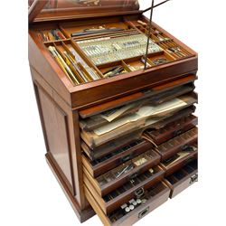 Edwardian mahogany artist's cabinet once belonging to the British artist Eli Marsden Wilson (1877-1965), raised panelled back mounted by carved brackets, sloped and hinged glazed lid enclosing paint holders and compartments, up-and-over panelled door revealing three slides, fitted with two banks of five graduating drawers with recessed brass handles, on skirted base.

Together with a quantity of artists' equipment and tools including paints, paintbrushes, charcoal, chalks, etc. and various prints relating to the life of the artist, including Quaker anti-war posters, Victorian Stevengraphs, and various chromolithographs 

Provenance: Removed from the studio of Eli Marsden Wilson. The cabinet comes to us for sale through family descent. The vendor is descendant of Marsden. Many further etchings removed from the cabinet are being sold in the Spring Art Sale, Friday 15th March 2024, Lots 265-271.

Notes: born in Ossett, Eli Marsden Wilson was the only son of Alfred Wilson, a foreman beamer, and Emma Marsden, and had five sisters. After studying at Wakefield College of Art, he moved to the Royal College of Art in London, where he became a pupil of Sir Frank Short. He had his first exhibit at the Royal Academy in 1905, the same year he married fellow artist Hilda Mary Pemberton.

A Quaker, vegetarian, and pacifist, he was a conscientious objector in World War I and as such was imprisoned in 1917 for two years. In September 1922 he was commissioned by Princess Marie Louise to produce miniature etchings for Queen Mary's Dolls' House at Windsor Castle; two such etchings are being sold in the Spring Art Sale, Friday 15th March 2024, Lot 265.